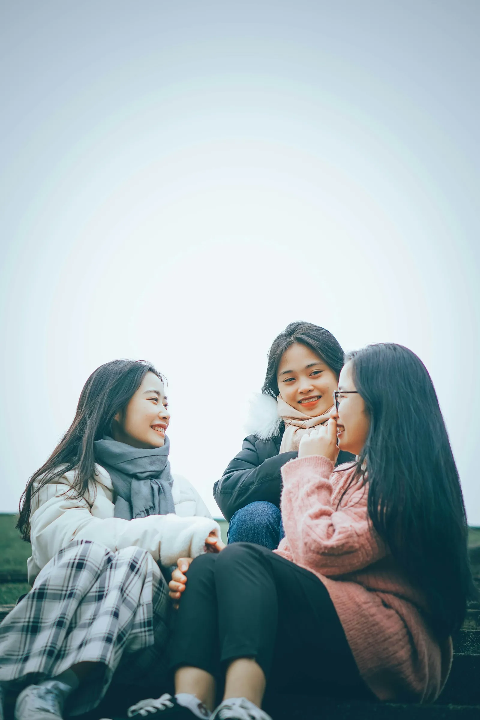three young women sitting on the ground laughing