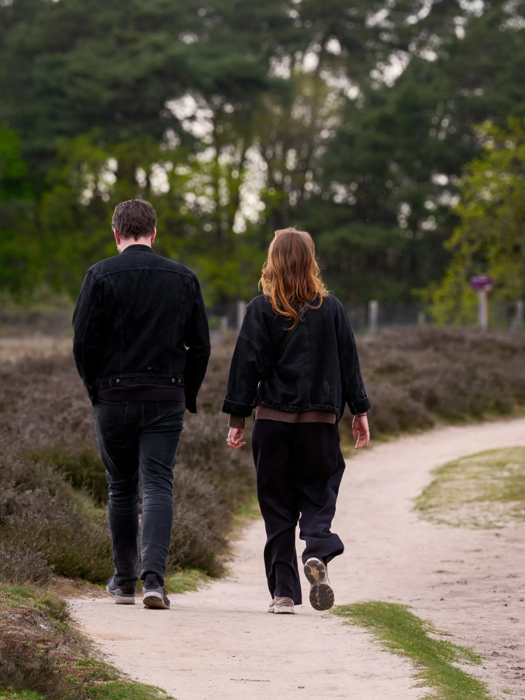 Two people walking on a dirt path through woods.