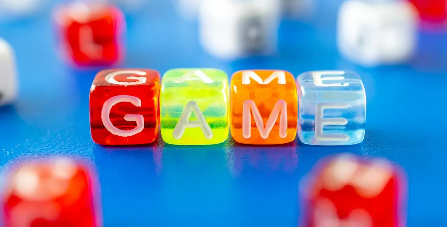 The word GAME spelled out with colorful plastic letter cubes on a blue surface